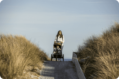 A woman is pushing a stroller on a road between grassy patches